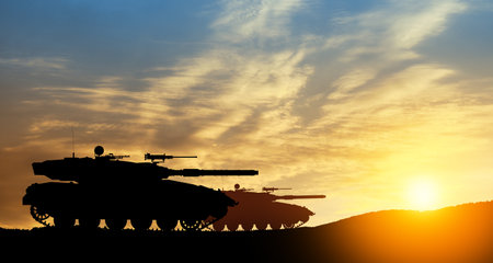 Silhouettes of army tanks at sunset sky background. Military machinery.の写真素材