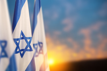 Israel flags with a star of David over cloudy sky background on sunset. Patriotic concept about Israel with national state symbols. Banner with place for text.の写真素材