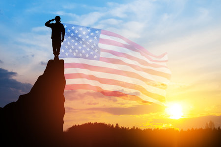 USA army soldier saluting on a background of sunset or sunrise and USA flag. Greeting card for Veterans Day, Memorial Day, Independence Day. America celebration.の写真素材