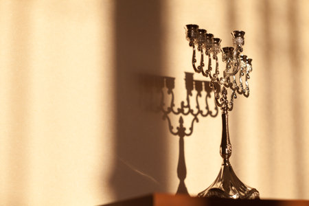 Hanukkah menorah, or hanukkiah in the light of the sun at sunset for Jewish holiday Hanukkah. Hanukkah lamp, nine-branched candelabrum without candles with a shadow on the wall.の写真素材