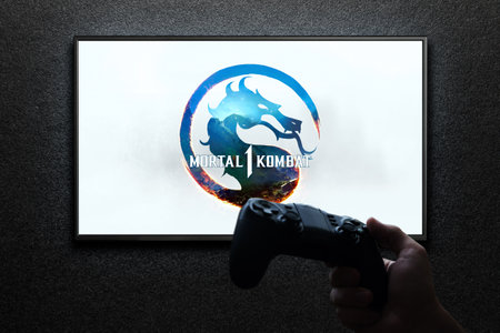 Mortal Kombat 1 game on TV screen with gamepad in hand on black textured wall with light. Astana,...
