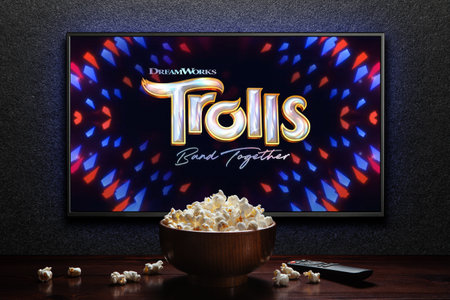 Trolls Band Together trailer or movie on TV screen. TV with remote control and popcorn bowl.のeditorial素材