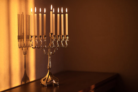 Hanukkah menorah, or hanukkiah in the light of the sun at sunset for Jewish holiday Hanukkah. Hanukkah lamp, nine-branched candelabrum with burning candles with a shadow on the wall.の写真素材