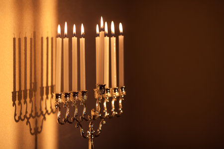 Closeup of Hanukkah menorah, or hanukkiah in the light of the sun at sunset for Jewish holiday Hanukkah. Hanukkah lamp, nine-branched candelabrum with burning candles with a shadow on the wall.の写真素材