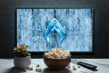 Aquaman and the Lost Kingdom trailer or movie on TV screen. TV with remote control, popcorn bowl and...