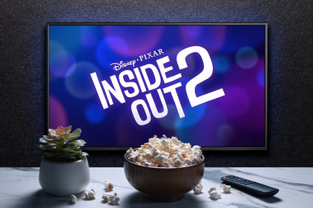 Inside Out 2 trailer or movie on TV screen. TV with remote control, popcorn bowl and home plant.のeditorial素材