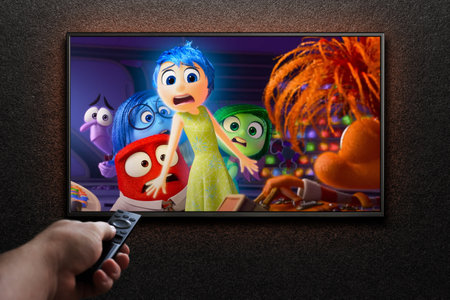 Inside Out 2 trailer or movie on TV screen. Man turns on TV with remote control.のeditorial素材
