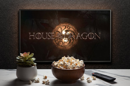 House of the Dragon trailer or movie on TV screen. TV with remote control, popcorn bowl and home plant.のeditorial素材