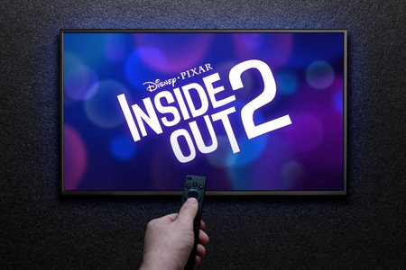 Inside Out 2 trailer or movie on TV screen. Man turns on TV with remote control.のeditorial素材