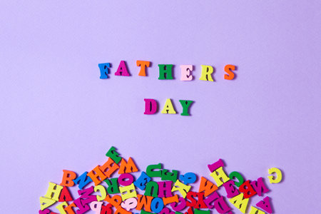 Childs toy letters spelling Fathers Day next to randomly lying letters on purple background.の写真素材