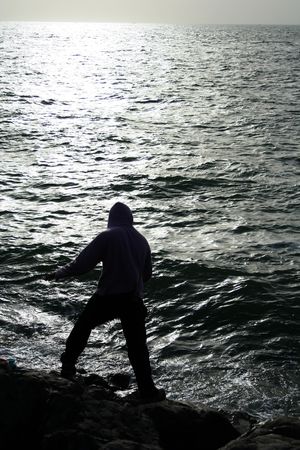 fisher man standing on rocks & waves of seaの写真素材