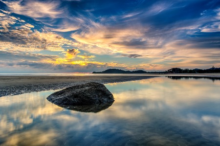 A beautiful reflection of rock at seaside during the sunrise timeの写真素材