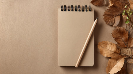 top view of notepad with pencil and dry leaves on beige backgroundの素材