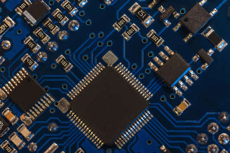 Close-up of a blue printed circuit board (PCB) with stripes of conductors between a transistor and...