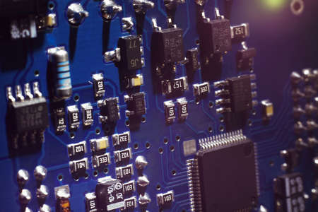 Close-up of a blue printed circuit board (PCB) with stripes of conductors between a transistor and an electronic equipment processor. IT technologies in programming, upgrade and abstract backgroundの写真素材