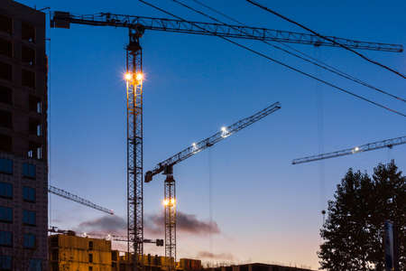 Close-up of a construction crane in the light of night lights on a modern site while working in new buildings. Night city landscape. Development conceptの写真素材