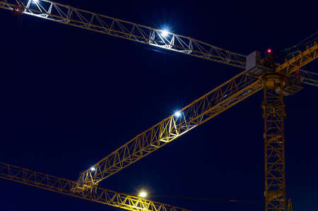 Close-up of a construction crane in the light of night lights on a modern site while working in new buildings. Night city landscape. Development conceptの写真素材