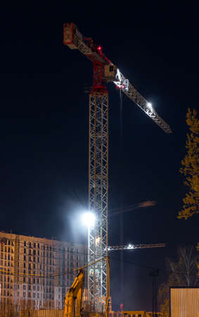 Close-up of a construction crane in the light of night lights on a modern site while working in new buildings. Night city landscape. Development conceptの写真素材
