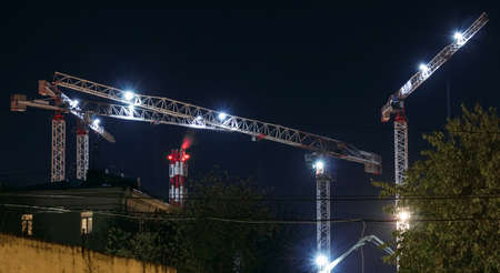 Close-up of a construction crane in the light of night lights on a modern site while working in new buildings. Night city landscape. Development conceptの写真素材