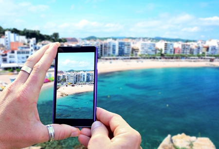 View over the mobile phone display during taking a picture of Costa Brava beach in Blanes town. Holding the mobile phone in hands and taking a photo. Focused on mobile phones screen.の写真素材