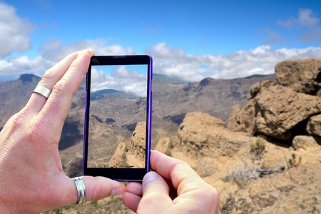 View over the mobile phone display during shooting Gran Canaria mountains. Holding the mobile phone in hands and taking a photo, focused on mobile phone screen.の写真素材