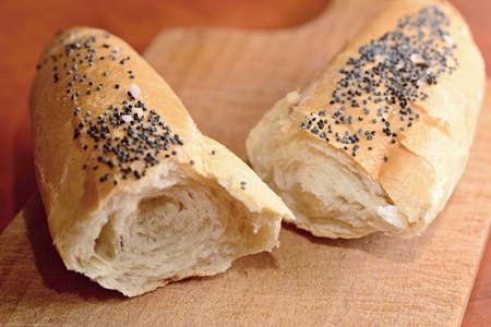 Two pieces of a white bread roll sprinkled with poppy seed and salt on a wooden cutting board.の写真素材