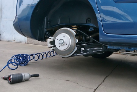 View of a disc brake during tyre replacement and pneumatic air screwdriver on the ground. Car...
