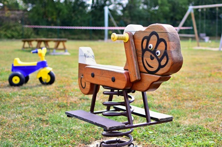 A close-up view of wooden swing on spring with plastic tricycle in the empty playground. Shallow depth of field. Focused on foreground.の写真素材