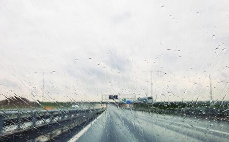 A view from car through window with rain drops during riding. Driving a car in the rain storm on highway.の写真素材