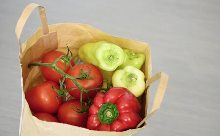 Top view of grocery paper bag full of tomatoes and green peppers on grey background.Full paper bag with vegetables.の写真素材