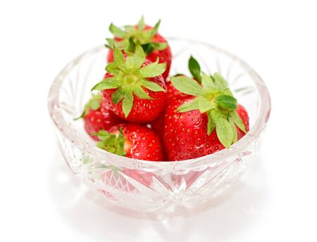 Heap of fresh strawberries in glass bowl over white background.の写真素材
