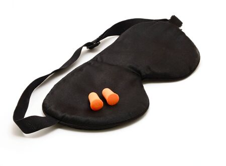 Black sleep eye mask with pair of orange foam ear plugs over white background.の写真素材