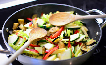 Stir fry fresh chopped eggplant, zucchini and peppers in the pan with wooden spoon. Preparing healthy food.の写真素材