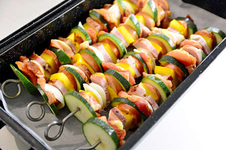 Pan full of metallic skewers with uncooked raw pork meat and vegetables ready for baking.の写真素材