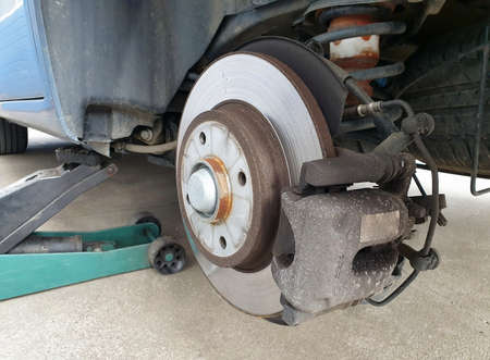 Close up of a car disc brake and a jack during car maintenance. Close up of disc brake without the wheel, car lifted on a jack.の写真素材