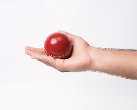 A Red Gleaming Leather Stitched Test Cricket Ball In Male Hand Closeup Photo On White Backgroundの写真素材