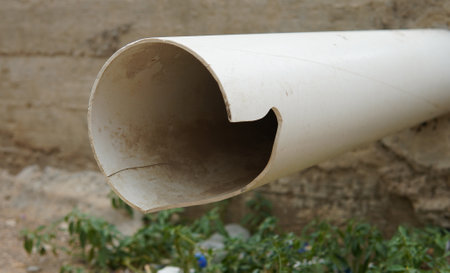 A Closeup Of An Irregularly Cut White PVC Pipe On A Concrete Wall Showing Wear And Greenery
