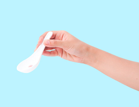 Clean white ceramic Asian spoon held by hand on a bright blue background.の写真素材