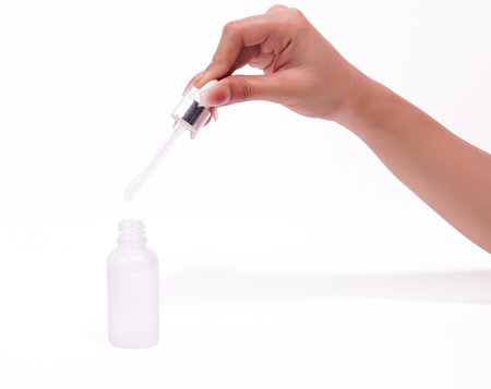 Hand dispensing liquid from a dropper into a skincare bottle.