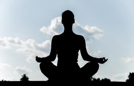 Pretty woman doing yoga exercises in the park. silhouette.の写真素材