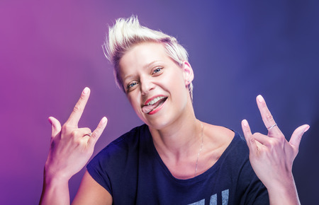 Portrait of a happy young woman doing rock symbol over color lights.の写真素材