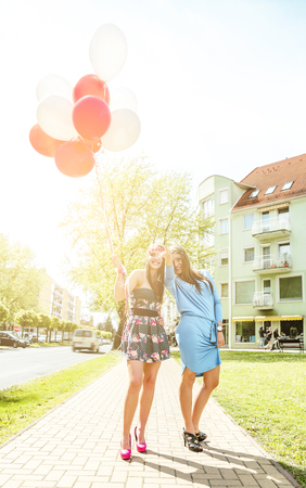 Two young blond women holding colorful latex balloons.の写真素材