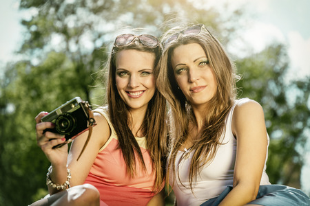 Two beautiful young women using a vintage camera in the street at summer.の写真素材