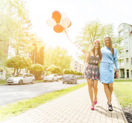 Two young blond women holding colorful latex balloons.の写真素材