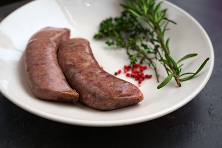 raw sausages for grilling in a white plate on a stone backgroundの写真素材