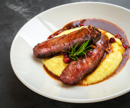 grilled sausages with mashed potatoes in a white plate on a stone backgroundの写真素材