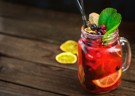 homemade lemonade in glass jar with ice, orange and berries in a tree on a black backgroundの写真素材