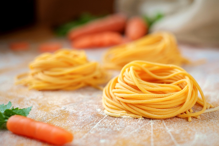 Fresh spaghetti sockets with carrots on the wooden table. Traditional Italian raw pastaの写真素材
