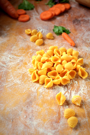 fresh homemade conchiglie pasta with carrots on a wooden tableの写真素材