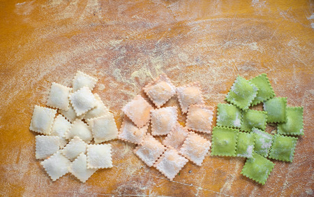 Multi-colored uncooked ravioli on a cutting board, sprinkled with flour, handmade, on a wooden table. Top view, copy spaceの写真素材